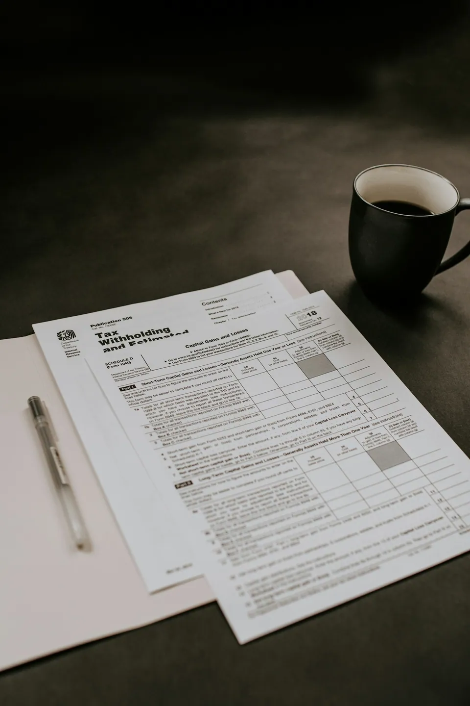 Tax forms and a pen beside a coffee cup on a dark table