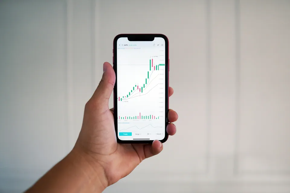 Hand holding a phone showing a candlestick chart