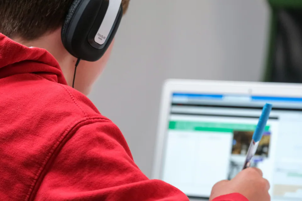 Person in headphones pointing a pen at a laptop screen