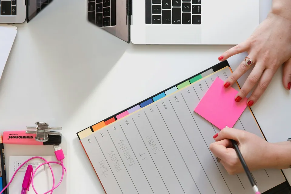 Overhead view of hands writing in a planner beside a laptop