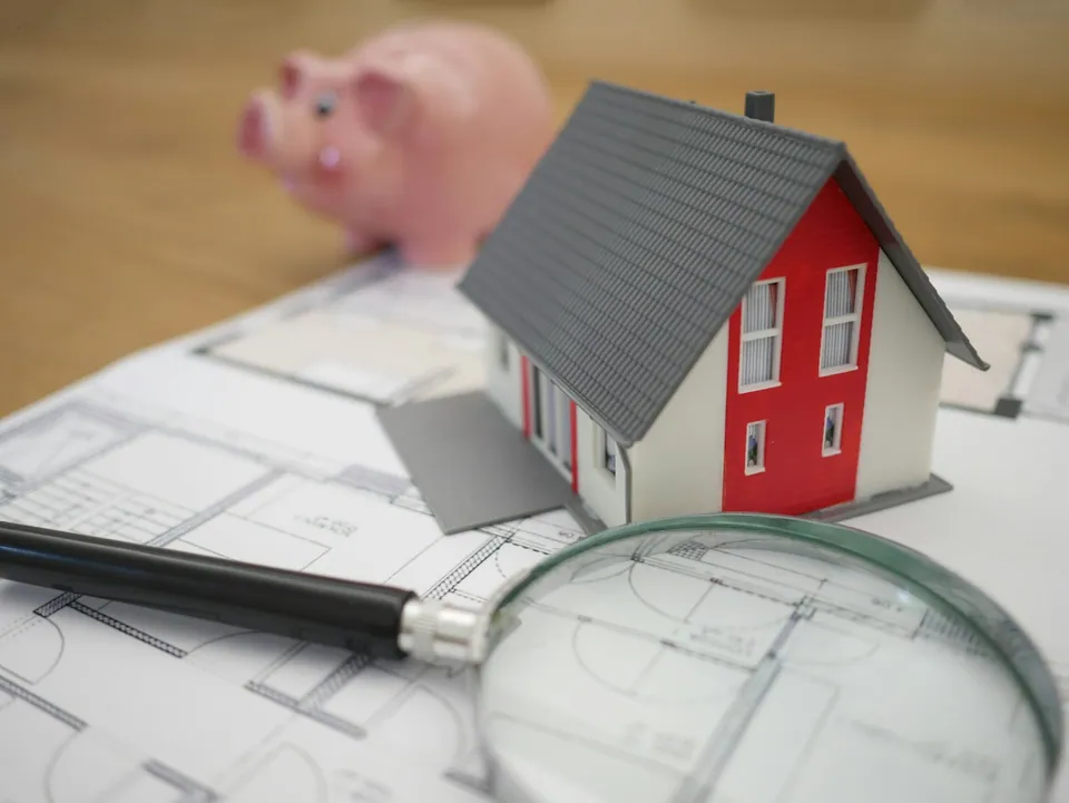 Model house with a piggy bank and magnifying glass on blueprints