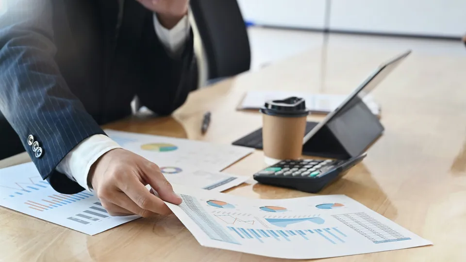 Businessman reviewing printed charts beside a tablet, calculator and coffee