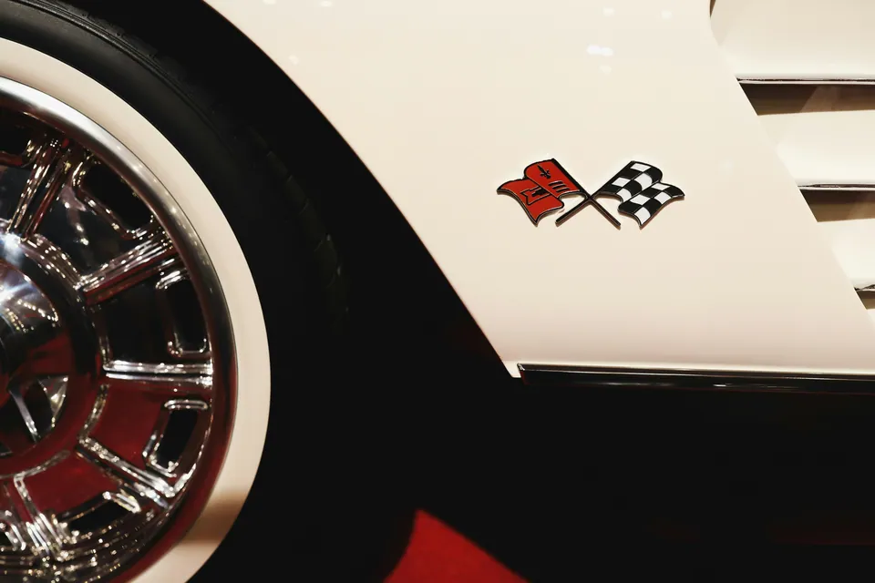 Crossed flags emblem on a white classic car beside a chrome wheel