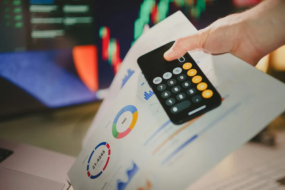 Hand holding a phone calculator over printed charts