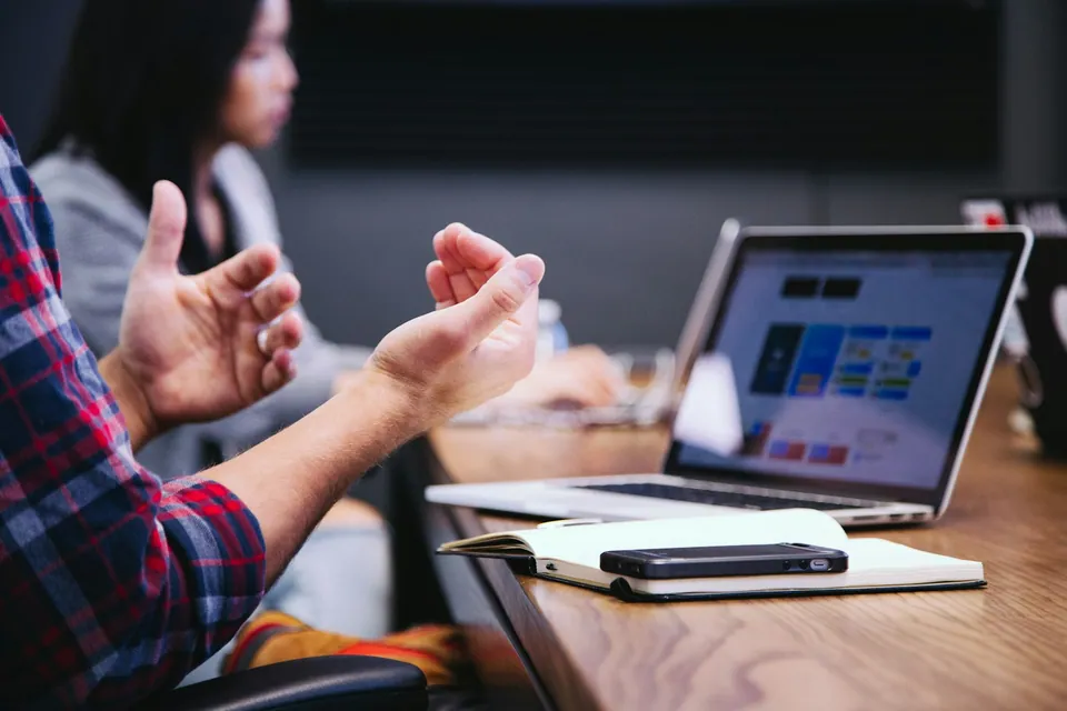 Colleagues talking with hand gestures at a table with laptops