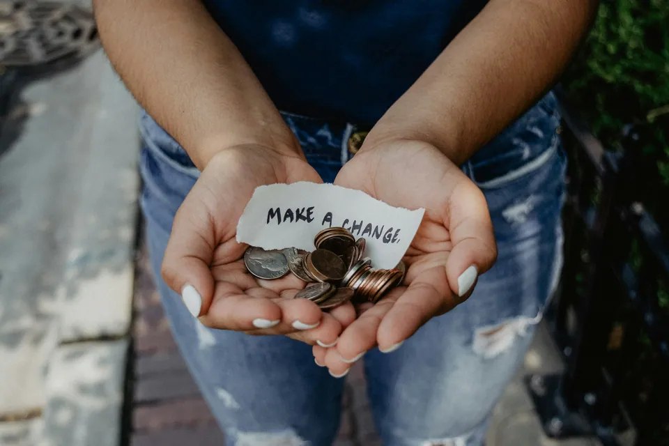 Cupped hands holding coins and a note reading Make a Change