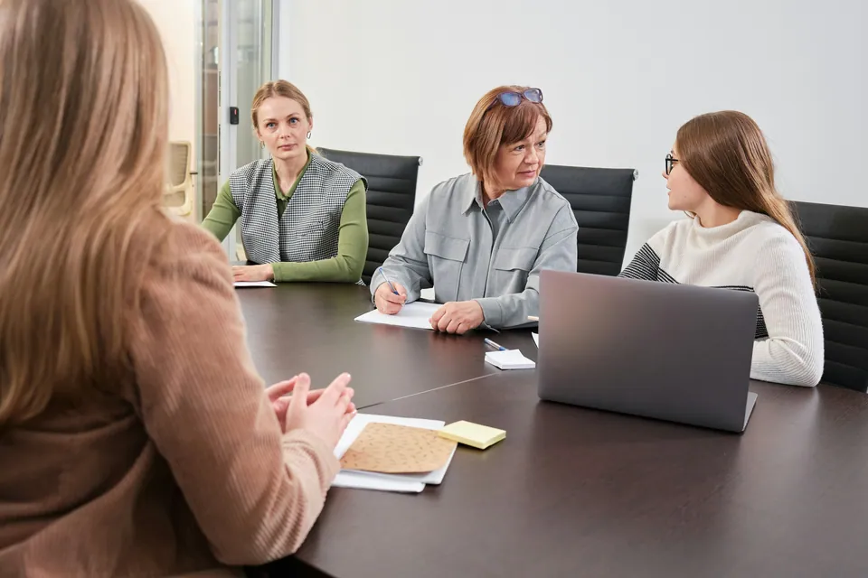 Four women in a meeting around a conference table with a laptop