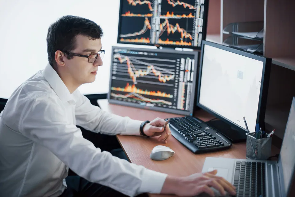 Trader in glasses working at several chart monitors
