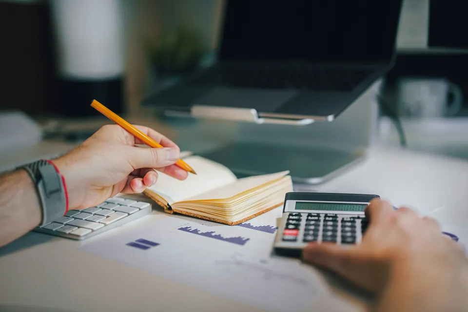 Hands with a pencil and calculator over a notebook and charts