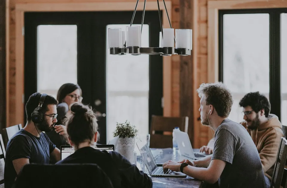 Team working on laptops at a long table in a wood-paneled office