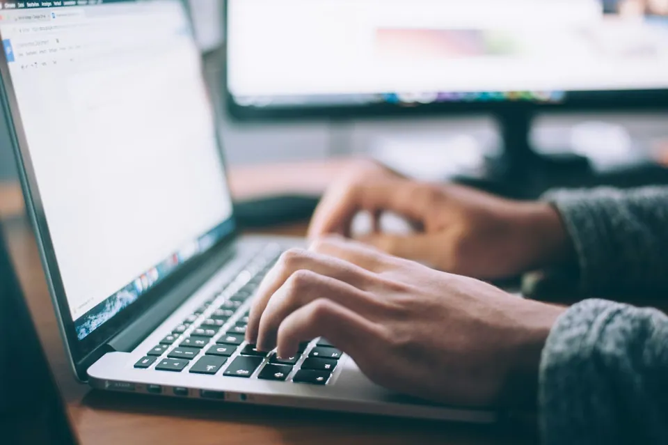 Hands typing on a laptop in a dim office