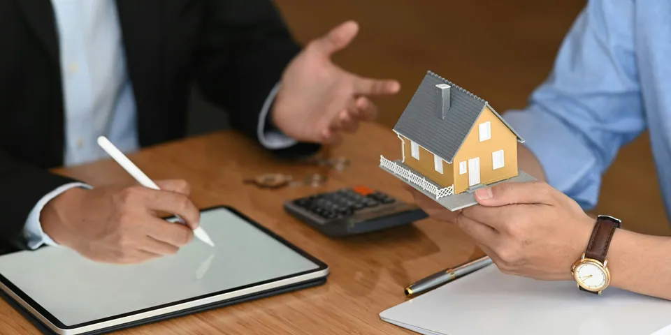 Advisor holding a model house while a client takes notes on a tablet