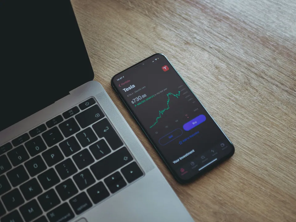 Phone showing a stock price app beside a laptop
