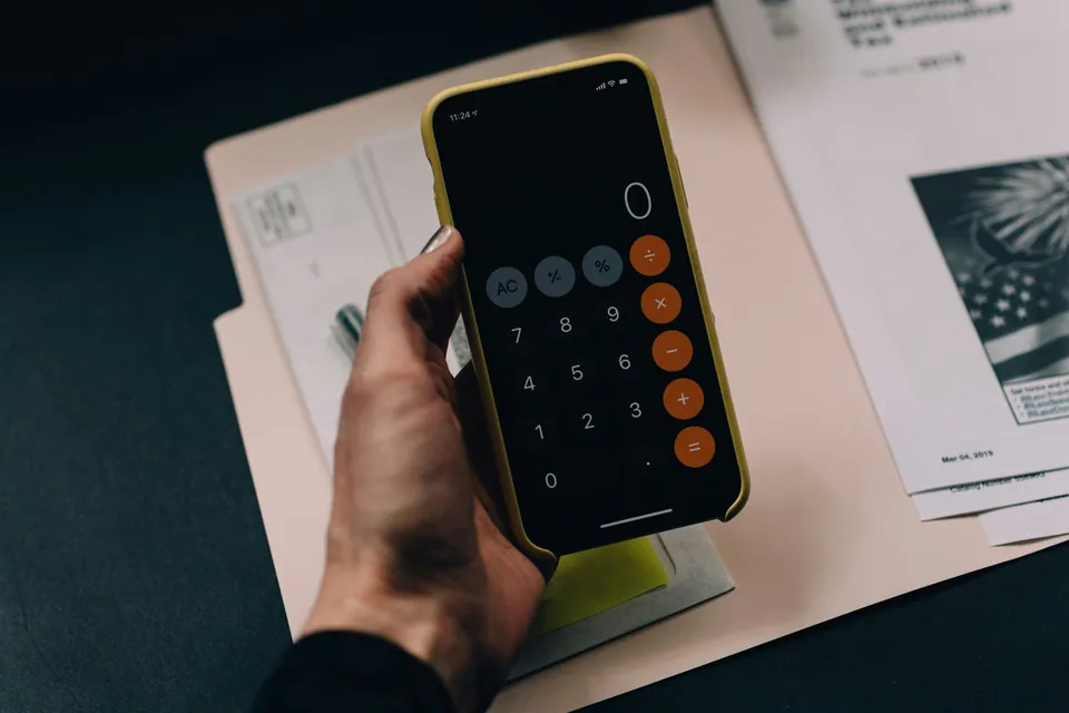 Hand using a phone calculator over a folder of tax documents