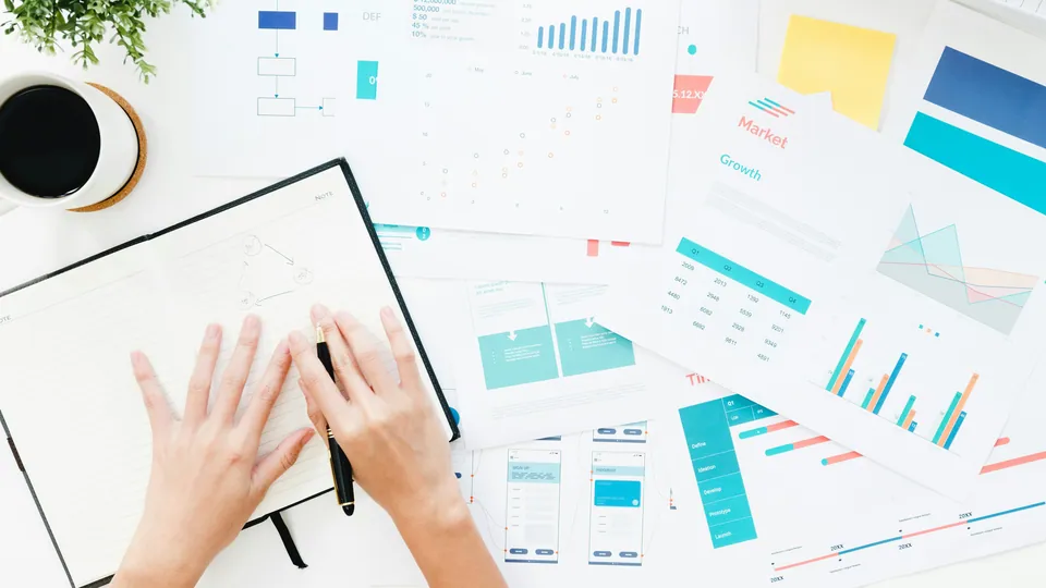 Hands over a notebook surrounded by printed charts and infographics