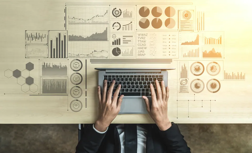 Overhead view of hands typing on a laptop surrounded by chart illustrations