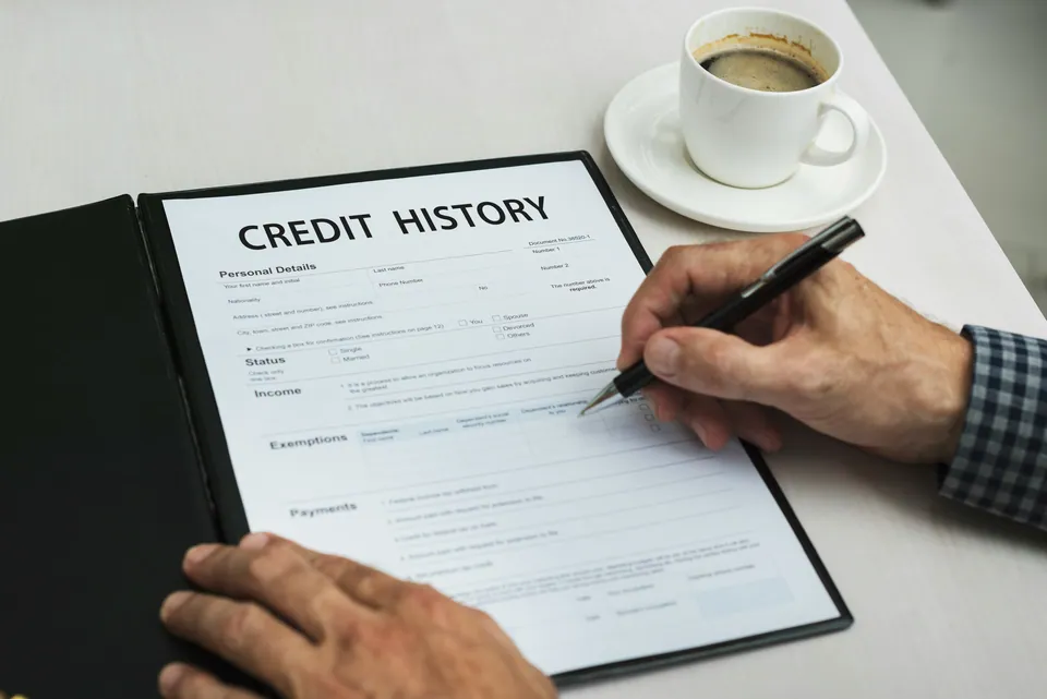 Hand filling out a credit history form beside a coffee cup