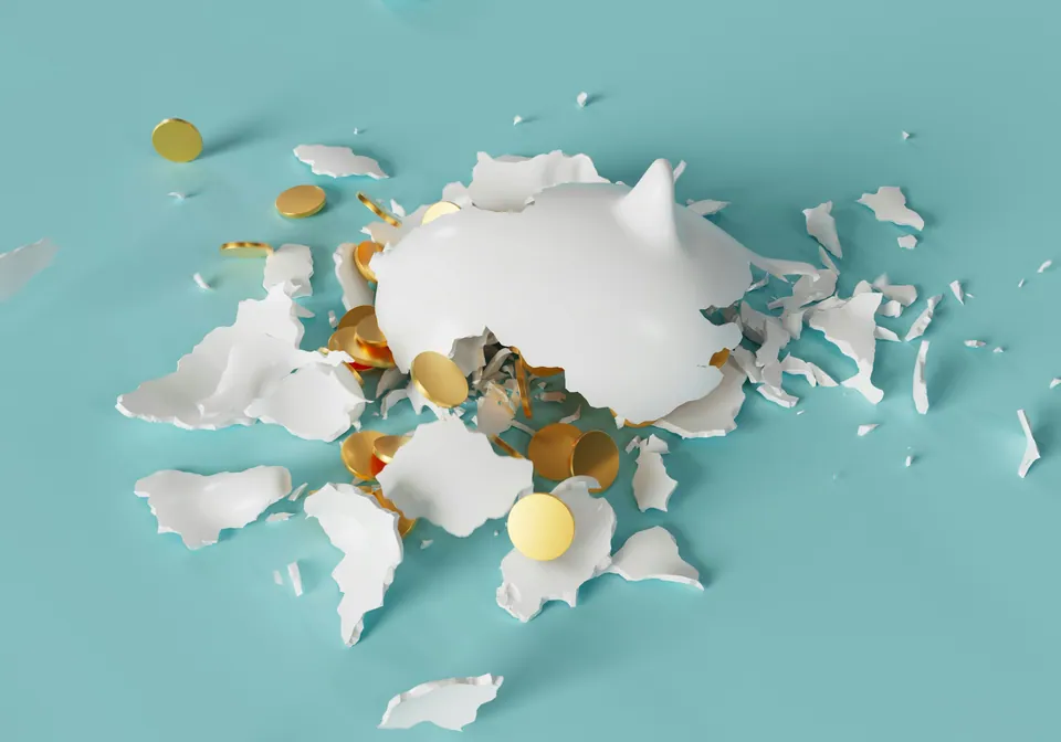 Shattered white piggy bank with gold coins on a teal surface