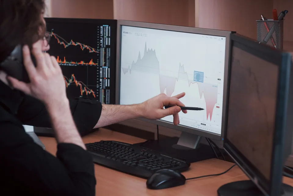Trader on the phone pointing at chart monitors