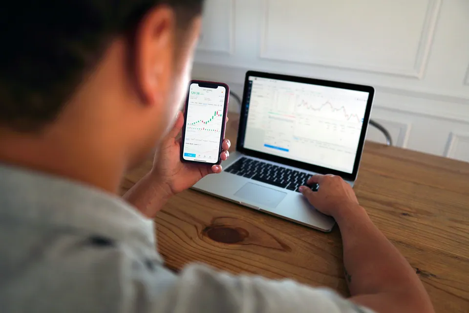 Person comparing a stock chart on a phone with a laptop