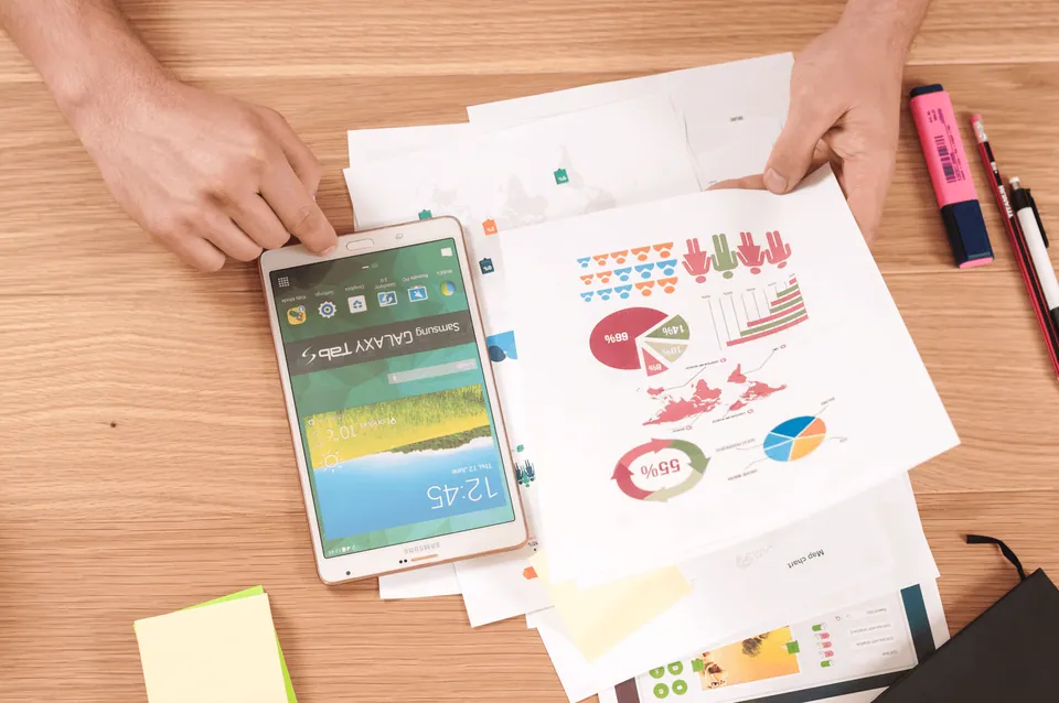 Hands holding a phone over printed infographic charts on a desk