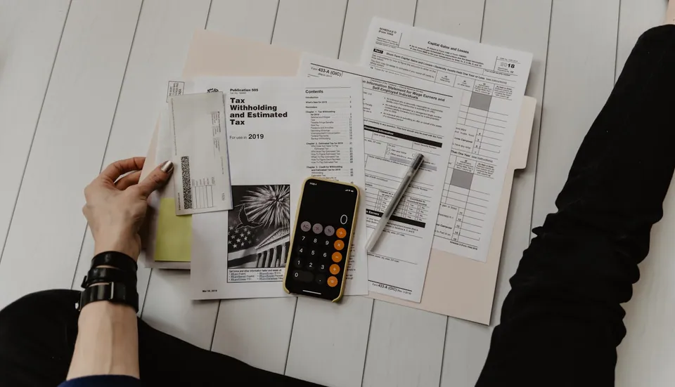 Hands holding tax forms beside a phone calculator on a white table