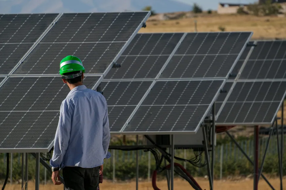 Engineer in a hard hat inspecting rows of solar panels