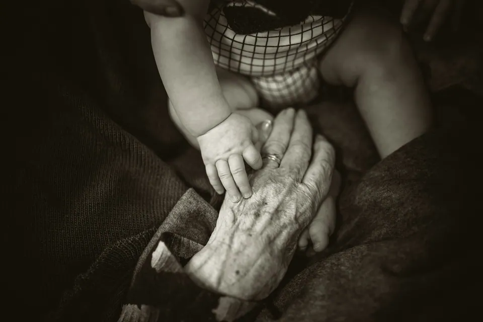 Black and white photo of a baby hand resting on an older hand