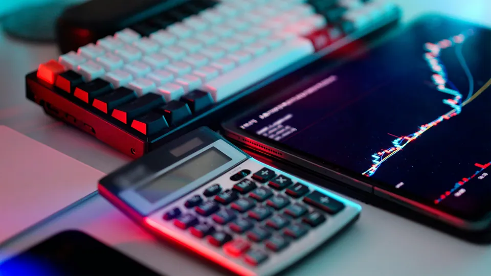 Calculator and keyboard beside a tablet showing a price chart