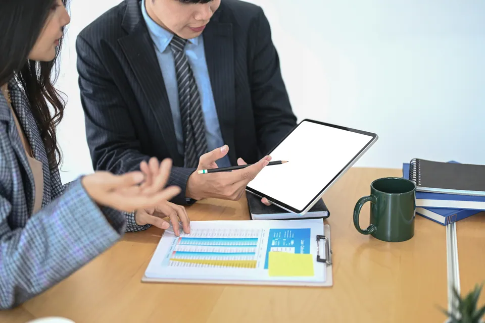 Two colleagues reviewing a tablet and printed report at a desk
