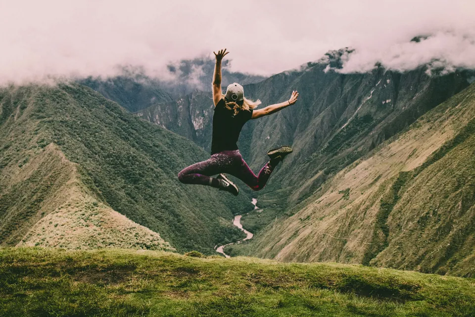 Hiker leaping in the air above a green mountain valley