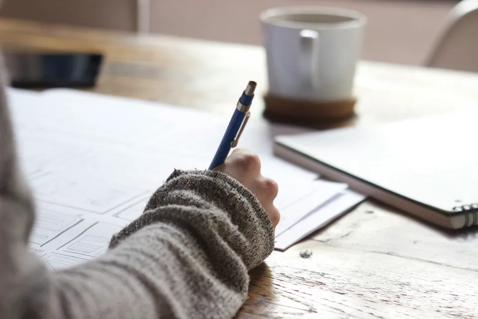 Hand writing notes beside a coffee cup at a wooden desk