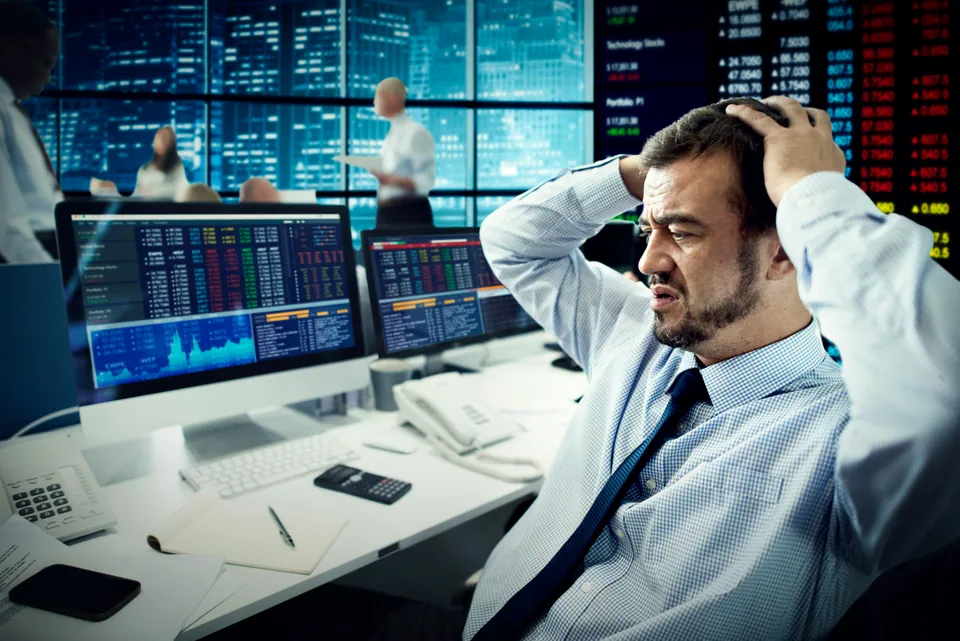 Stressed trader holding his head in front of market screens