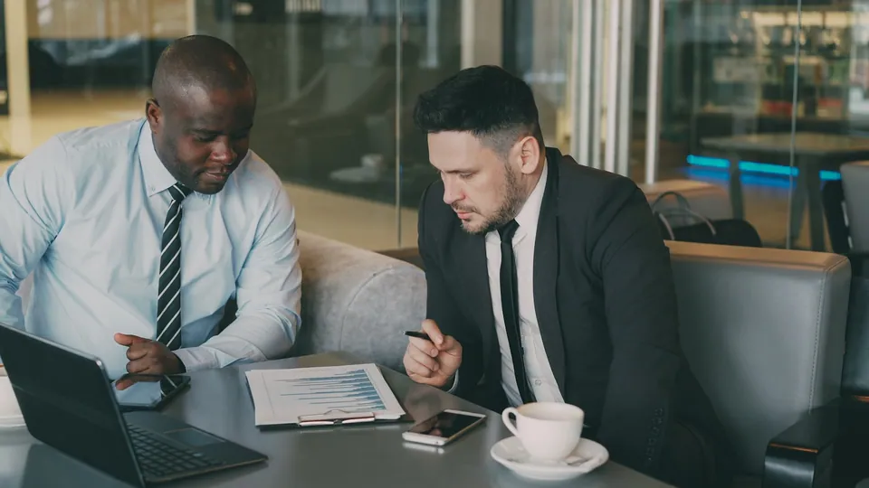 Two businessmen reviewing documents with a laptop on a sofa