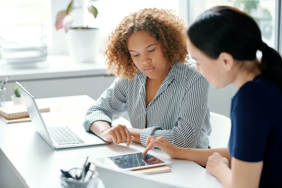 Two women reviewing figures on a tablet at a desk