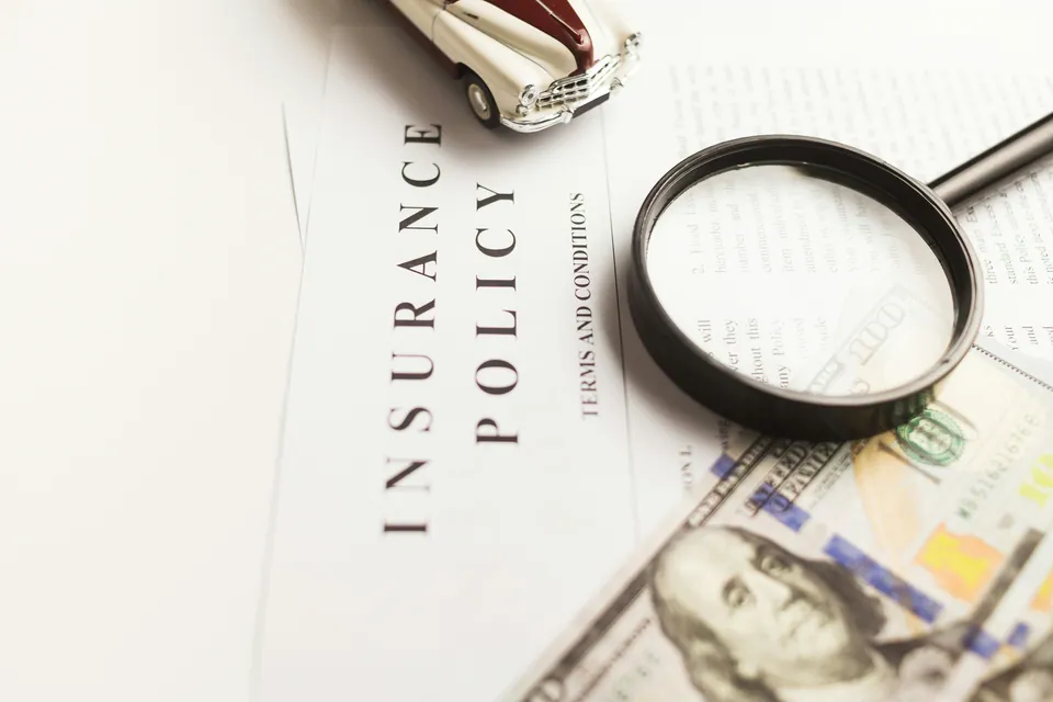 Insurance policy document with a magnifying glass and dollar bills
