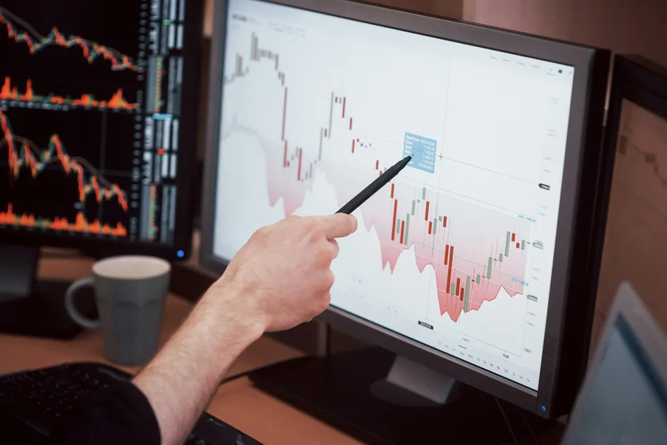 Hand pointing a pen at a candlestick chart on a monitor