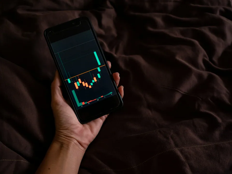 Hand holding a phone showing a candlestick chart in the dark