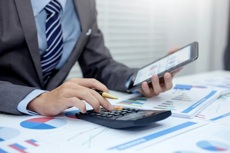 Businessman using a calculator and tablet over printed charts