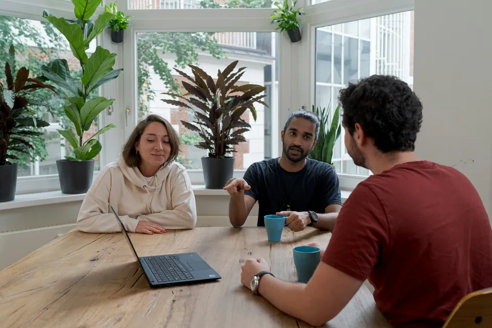 Three colleagues chatting at a table in a bright plant-filled office
