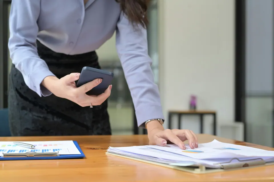 Woman using a phone calculator over documents on a desk