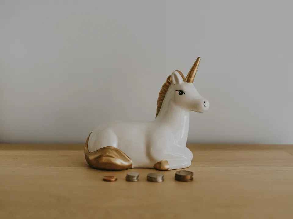 White unicorn figurine beside a few stacked coins