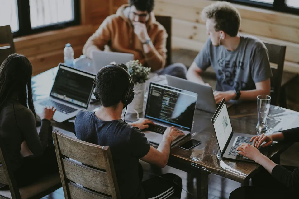 Developers working on laptops around a wooden table