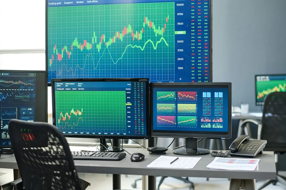 Trading desk with multiple monitors showing green charts
