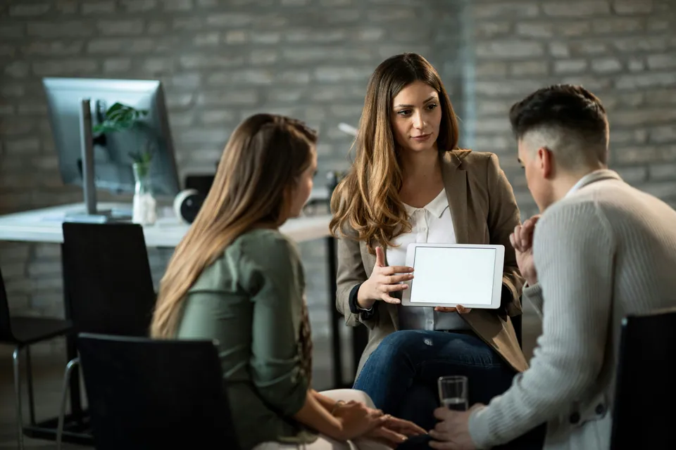 Three colleagues talking over a tablet in a brick office