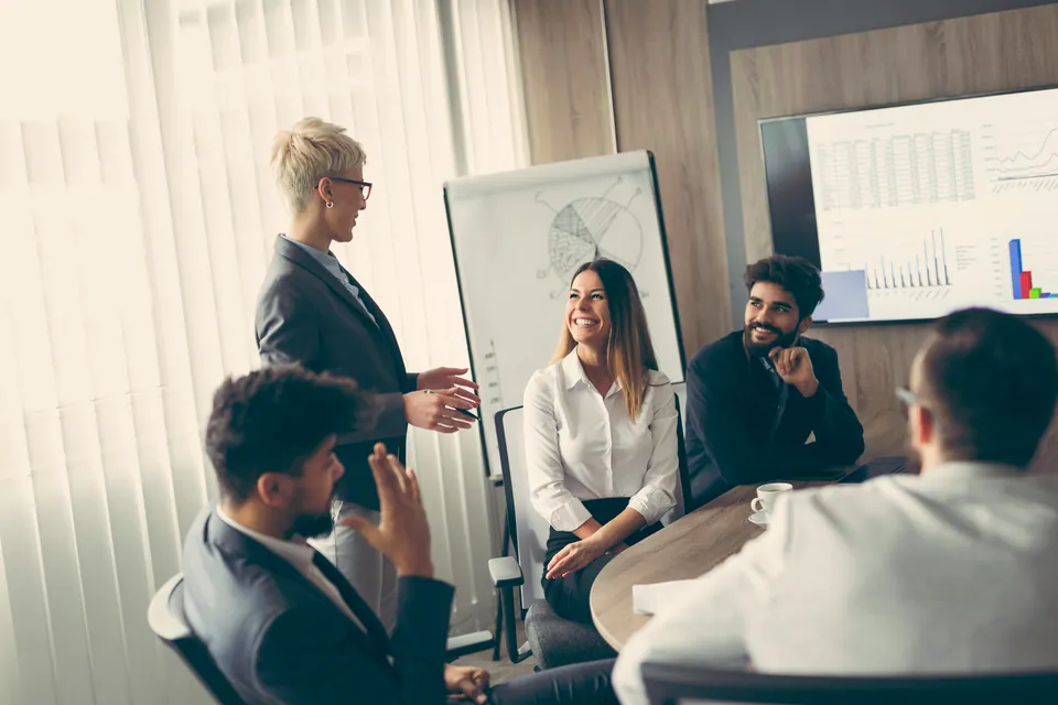 Woman presenting to smiling colleagues in a meeting room