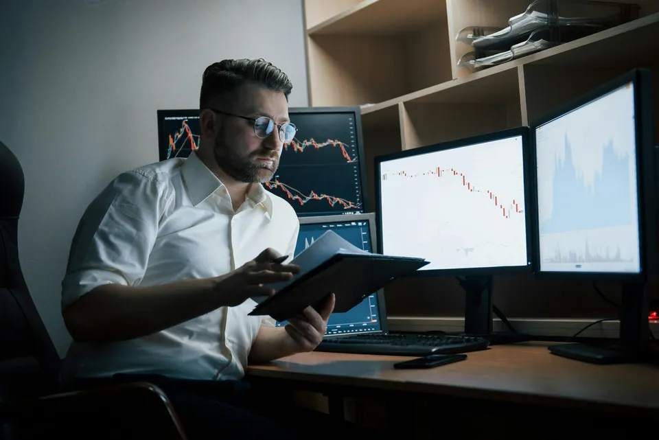 Trader reviewing a tablet in front of multiple chart monitors