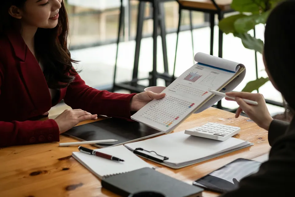 Two women reviewing a printed report with a calculator at a desk