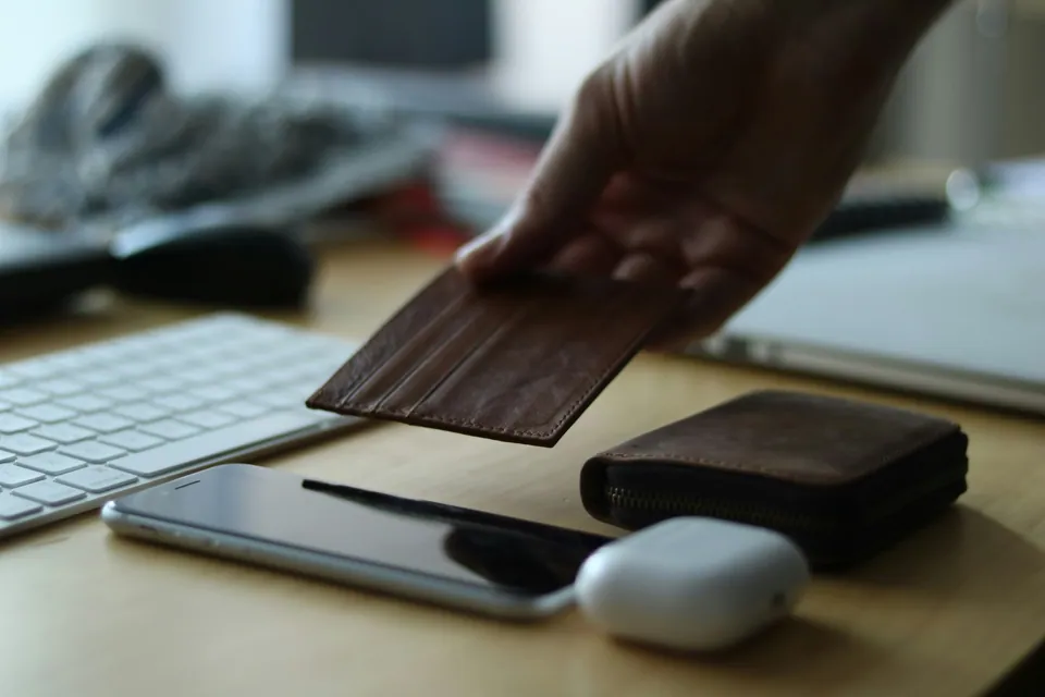 Hand placing a wooden card on a desk next to a wallet and phone