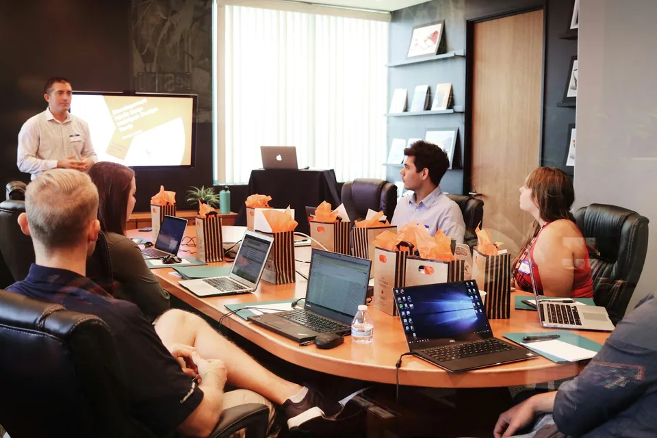 Presenter speaking to a team at a conference table with laptops